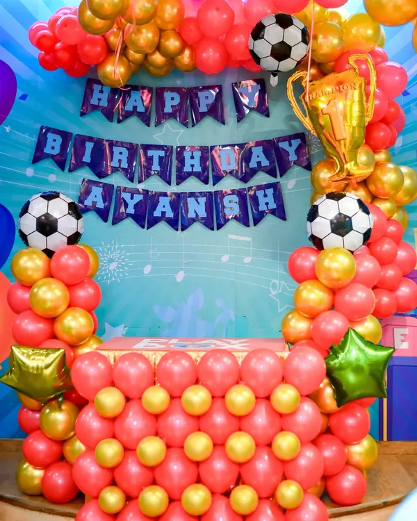 A vibrant football themed birthday setup. This includes a personalized "Happy Birthday" banner, a balloon arch in team colors, and trophy decorations.