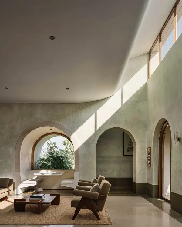 A living space at the DUA Villa, where a shaft of light from a high window illuminates the curved, lime-plastered walls. The interplay of grand volumes and intimate, carved-out niches is a hallmark of this project.