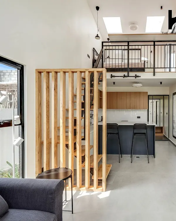 The interior of a 550 sq. ft. prefab home, showcasing a double-height living area with a mezzanine level. The open-plan design includes a modern kitchen, living space, and a staircase leading to the loft bedroom.
