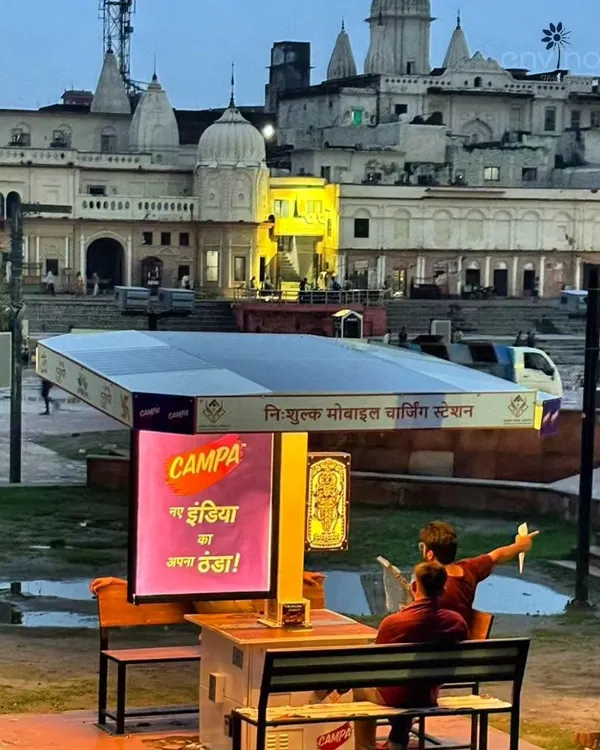 Our Smart Solar Hut at Saryu Ghat in Ayodhya, providing a moment of rest and connectivity for visitors against the backdrop of the serene evening landscape. The integrated digital screen displays a vibrant advertisement for Campa, demonstrating how brands can connect with audiences in high-footfall, culturally significant locations.