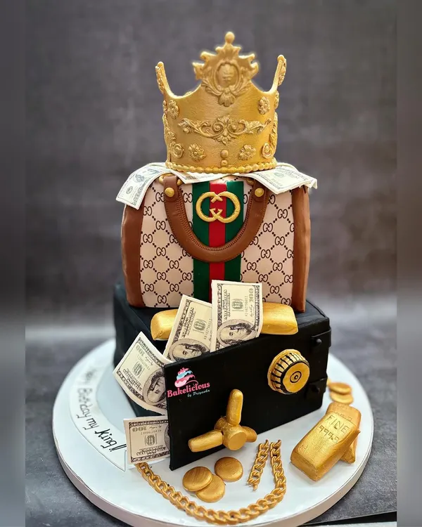 This two-tier luxury cake was designed for a wife to celebrate her king. It features an edible Gucci-inspired handbag, a money-filled safe, and gold accents, all handcrafted from fondant with a rich chocolate truffle flavour inside.