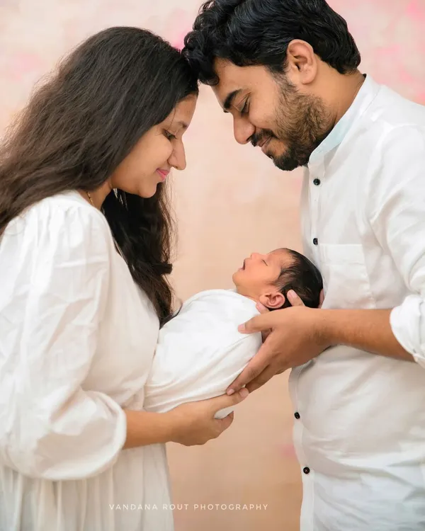 An intimate portrait of new parents with their newborn, their heads touching as they admire their baby. This pose is perfect for capturing the deep connection and love in a new family.