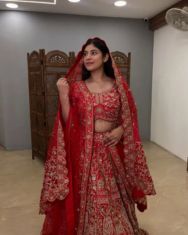 A side profile of a classic red bridal lehenga, showing the beautiful drape of the dupatta with its heavily embroidered border. This pre-loved piece is a smart choice for your big day.