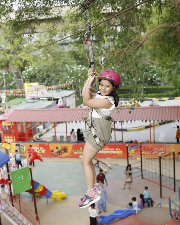 A clear, joyful shot of a child ziplining high above the park. You can see the excitement on her face as she glides through the air, fully secured in her harness.