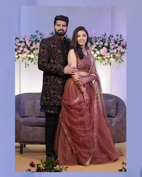 A classic full-length portrait of the couple at their reception, looking elegant and happy against a floral backdrop.