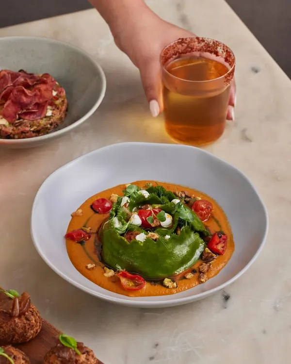This is one of our most popular bowls: the Spinach and Ricotta Crown Ravioli. The unique shape holds a delicate filling, perfectly complemented by a charred tomato and miso sauce, toasted walnuts, and creamy goat's cheese.