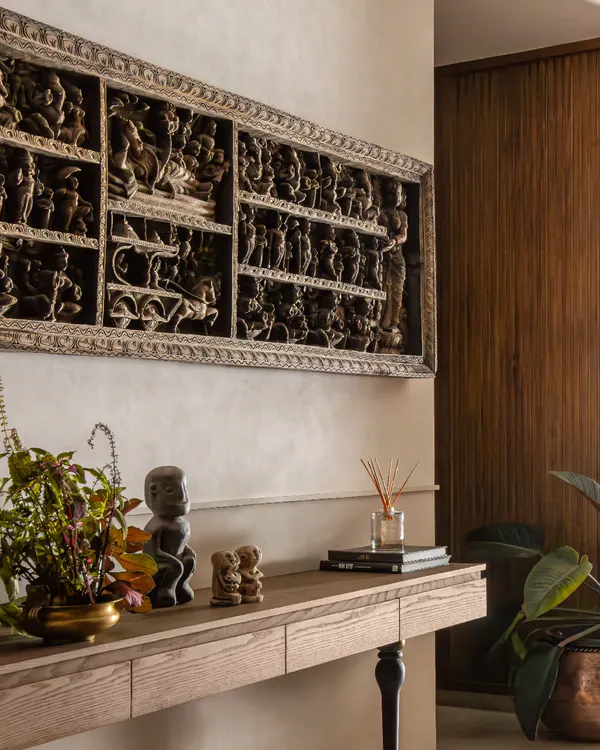 The foyer of The Collector's Retreat immediately introduces the home's narrative. A significant carved panel from the client's collection is the focal point, grounded by a simple console and warm wood paneling.