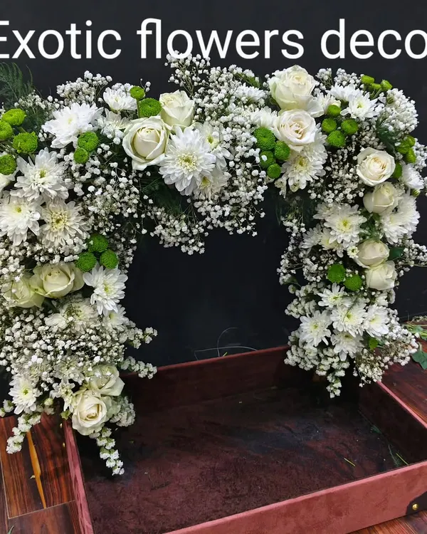 A large floral arch designed for event decor or as a frame for a gift hamper. This piece is crafted with white roses, chrysanthemums, and baby's breath, creating a lush and impressive display.