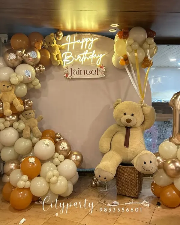 A complete view of our teddy bear themed first birthday decor, including the balloon arch with small teddy bears, a large bear prop holding balloons, and a custom number '1' balloon stand.