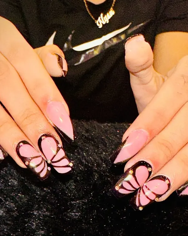 A close-up of my popular butterfly design. I use a sheer pink base on stiletto nails and hand-paint these delicate wings, outlined in black with tiny gold stud details for a touch of sparkle.