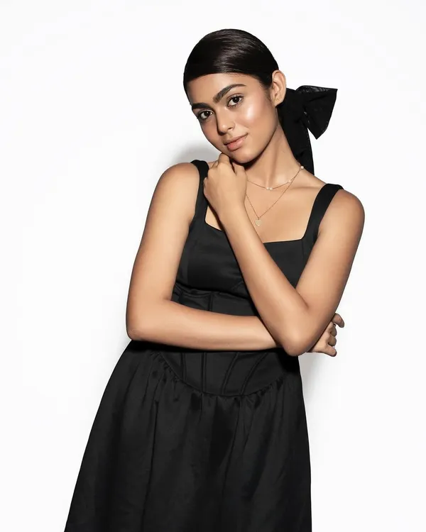 A chic and modern look featuring a sleek ponytail with a large bow accessory. The makeup is dewy with a nude lip, perfect for brown skin tones.