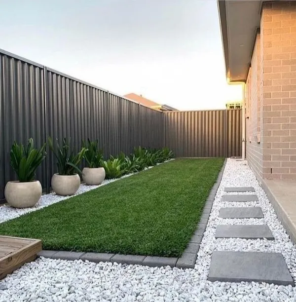 A modern and minimalist garden path created with rectangular stone pavers set in a bed of white pebbles. This design is not only visually clean but also low-maintenance and effective for drainage.
