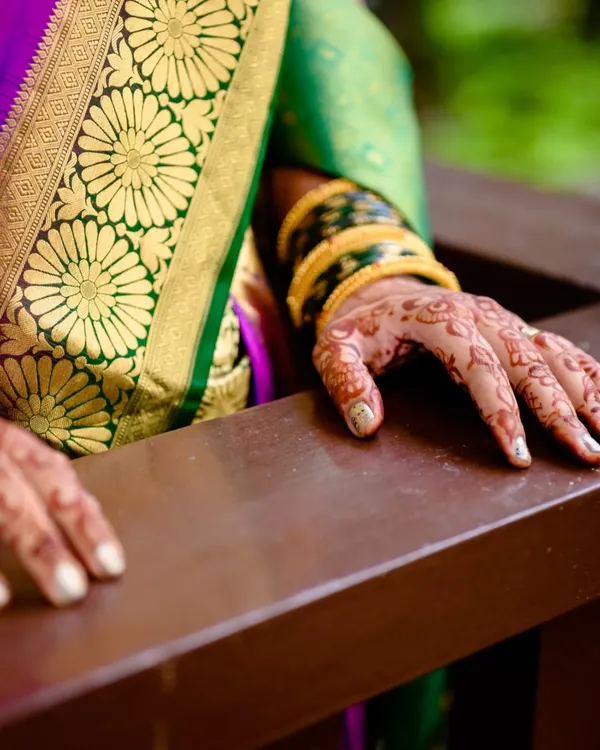 A close up of the bride's hands, showcasing her beautiful mehendi and traditional green bangles against the rich texture of her saree. These details are an essential part of the bridal look.