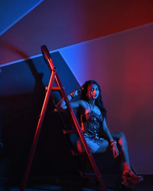 A shot that screams confidence. The ladder, the pose, the red and blue lighting, it all comes together to create a powerful, edgy look.