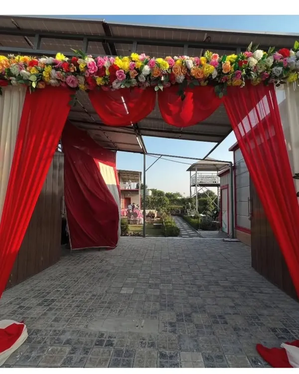 A beautiful floral archway to welcome guests to the wedding venue. The entrance is decorated with red and white drapes and topped with a border of colorful fresh flowers.