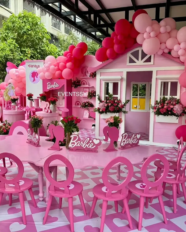 A full view of the ultimate Barbie party, featuring a custom dreamhouse, themed tables and chairs, and an abundance of pink balloons.