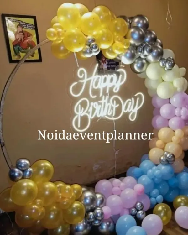 A circular ring backdrop with a 'Happy Birthday' neon sign and a colorful balloon garland is a popular choice for birthday parties and can be customized with any color scheme.