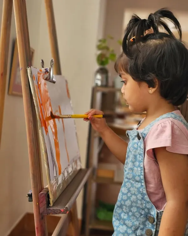 A young artist lost in her work at the easel. We provide open-ended art materials so children can explore colors, textures, and their own creativity without a predetermined end product.