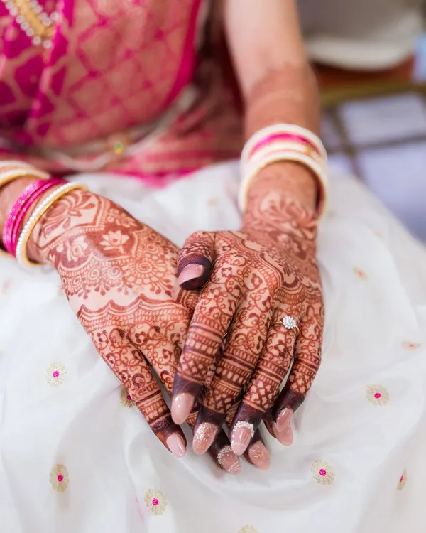 A close-up of the bride's hands, showcasing the beautiful, intricate patterns of her bridal mehndi and her engagement ring.