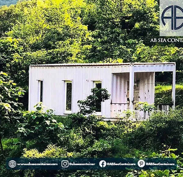 This minimalist container home is nestled in a lush, green landscape, offering an off-the-grid living experience. Its simple white exterior contrasts beautifully with the natural surroundings.
