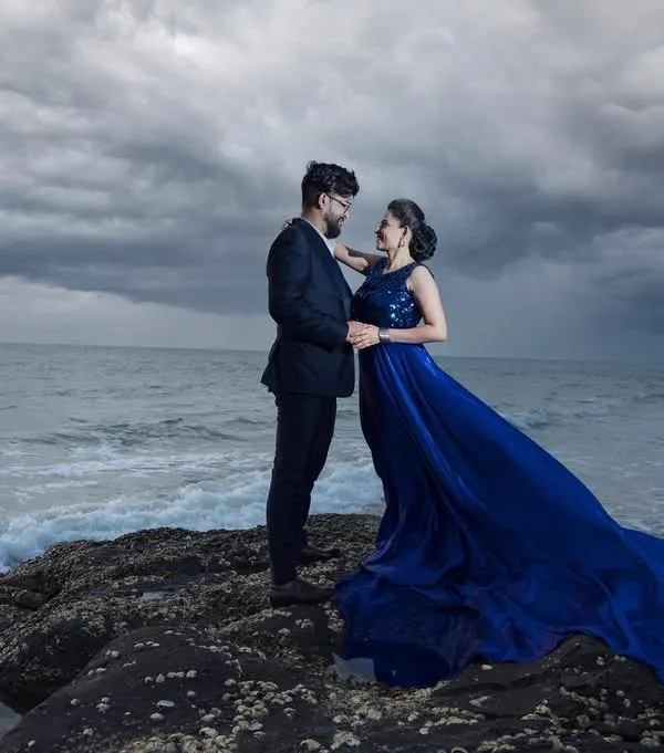 A dramatic coastal portrait with a stormy sky. The deep blue of the gown against the moody sea creates a powerful and cinematic image, perfect for couples who love a bit of drama.