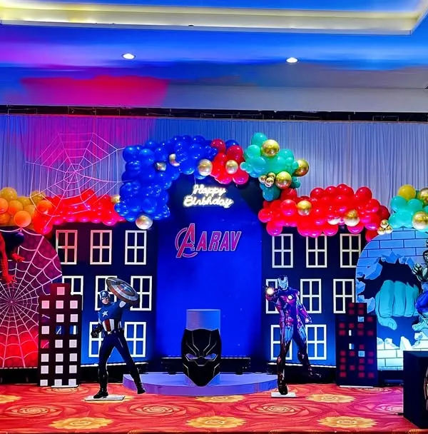 Avengers assemble for Aarav's 5th birthday. This superhero stage features a city skyline backdrop, character cutouts of Black Panther and Vision, and themed props like Iron Man's helmet and Captain America's shield.