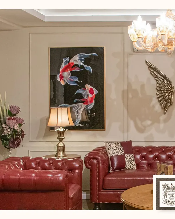 The Chesterfield sofa is the epitome of timeless design. Here, in a bold red leather, it anchors the room with confidence and character, complemented by the serene koi fish art and classic gold accents.