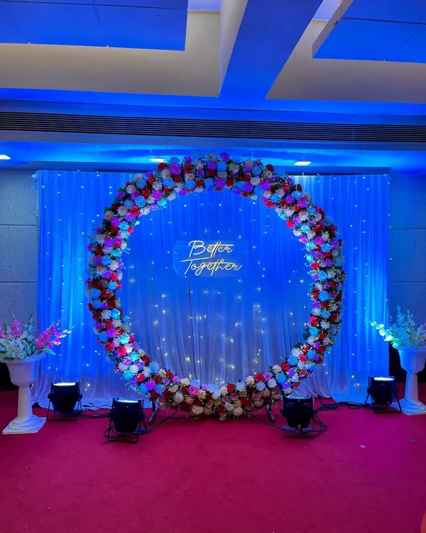 This large floral ring backdrop was designed for an engagement ceremony. The combination of red, pink, and white flowers, a 'Better Together' neon sign, and professional lighting creates a beautiful stage for the couple.