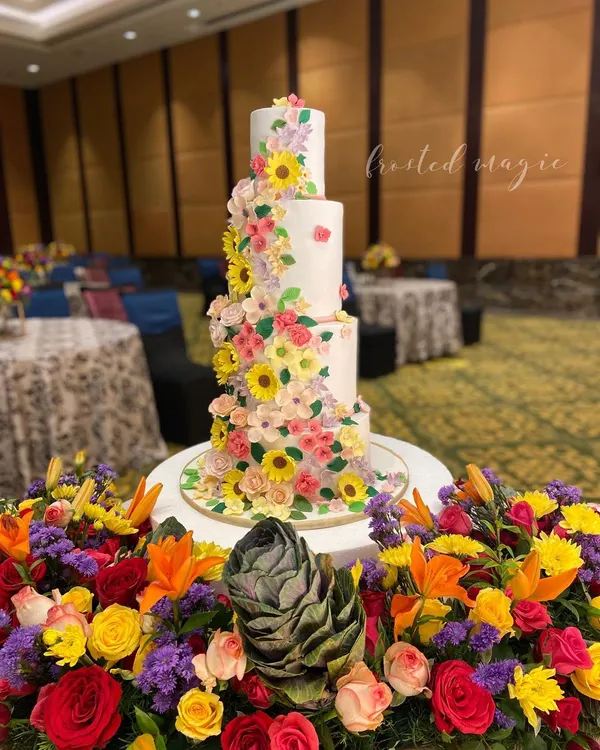 This four-tiered floral wedding cake was designed to match the vibrant flower decor of the event. It features a cascade of handmade sugar flowers, including sunflowers and cosmos, creating a stunning and cheerful centerpiece.