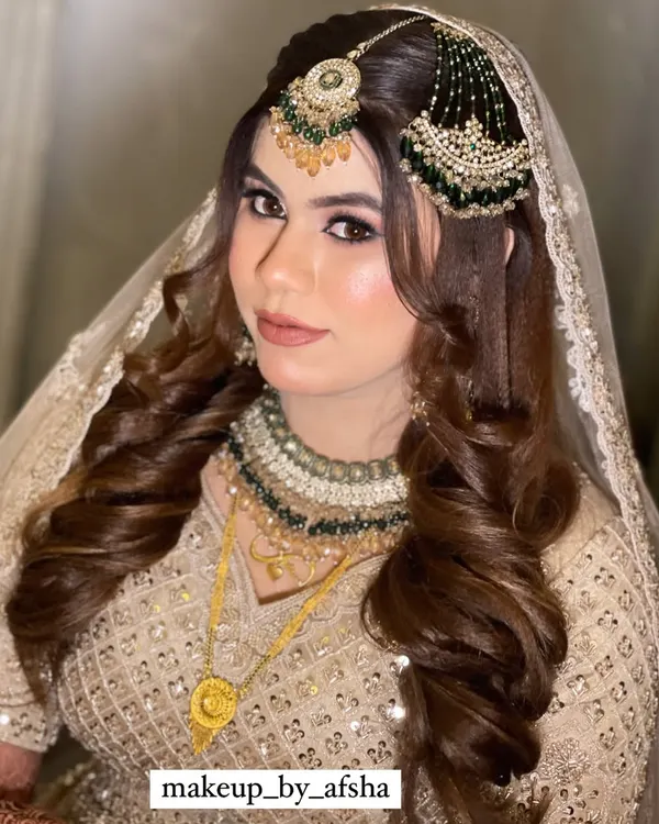 This bride's look is pure elegance. Her beige and green lehenga is paired with a soft glam makeup look, featuring voluminous curls and a perfectly placed maang tikka and passa.