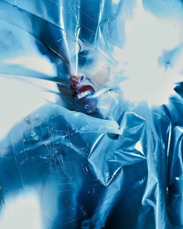 An intense, conceptual shot using plastic wrap to create a feeling of suffocation and struggle. The harsh, blown-out light from behind adds to the chaotic and raw emotion of the image.