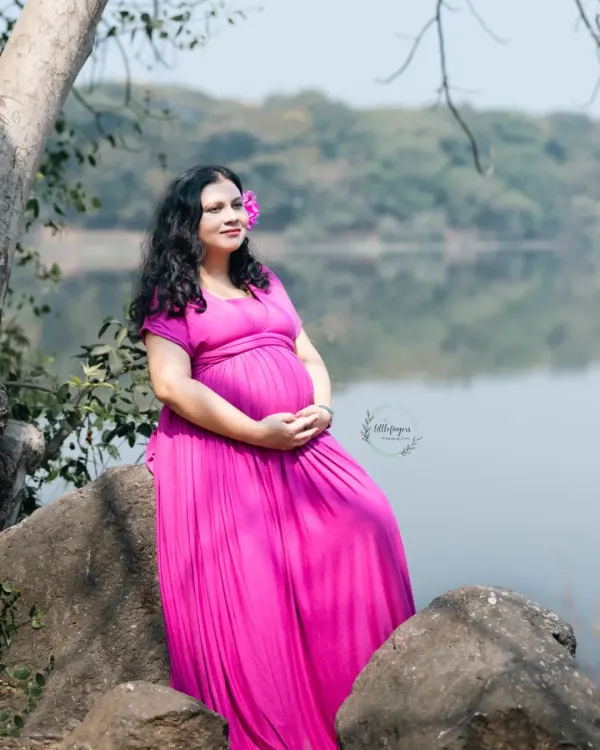 A moment of quiet reflection by the water. The mom-to-be, dressed in a vibrant pink gown, looks out at the horizon, embodying the peaceful anticipation of motherhood.