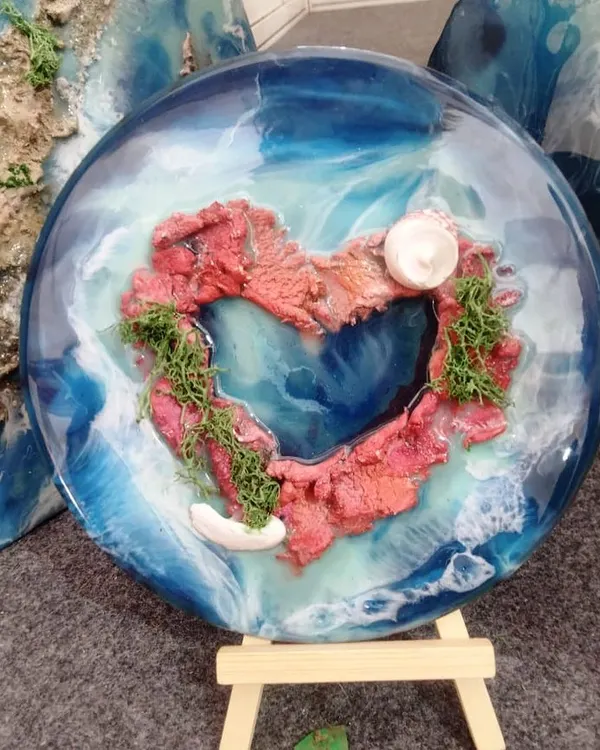 A custom "Lover's Island" resin piece. The heart-shaped island is surrounded by swirling blue resin waves, making it a perfect personalized gift to capture a romantic memory.