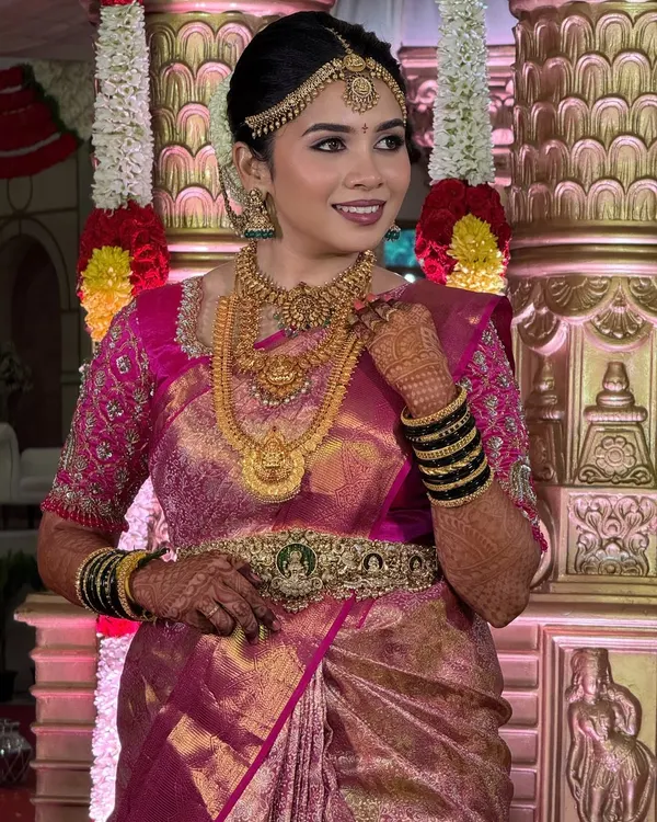 A radiant bride on her special day. This look features a soft glam finish that feels like a gentle breeze, perfectly complementing her pink silk saree and the divine temple setting.