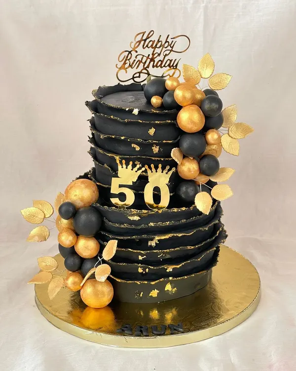 Turning 50 in style! This bold black and gold cake makes a glamorous statement with its textured finish, golden orbs, and regal crown details.