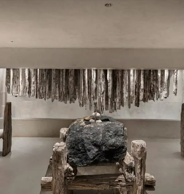 This space in the 'La Solitaire' showroom is a dialogue between stone, wood, and silence. The raw, unfinished textures of the furniture and the massive central stone create a powerful statement of minimalist, nature-inspired design.