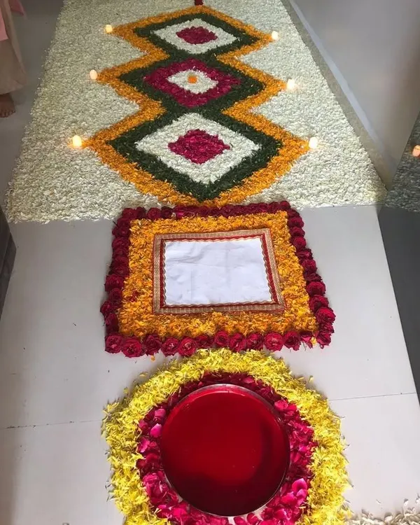 We specialize in detailed floral floor art, known as rangoli. This piece features intricate geometric patterns created with fresh petals of marigold, rose, and jasmine, with small diyas placed to add a warm glow.