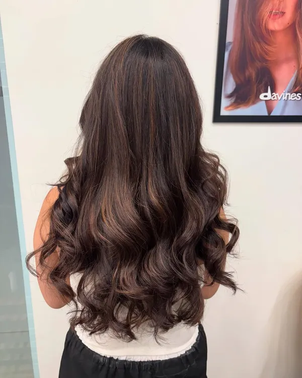 A back view of a rich brunette balayage, styled into voluminous waves. The subtle highlights add depth and movement to the hair.