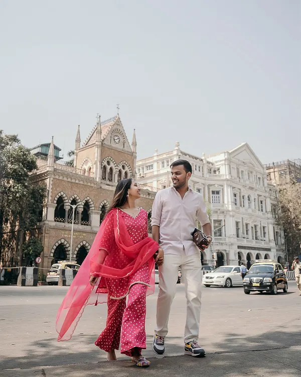 A classic Mumbai pre-wedding shot, with the couple taking a stroll against the backdrop of historic architecture. Her vibrant pink suit adds a beautiful pop of color to the city scene.