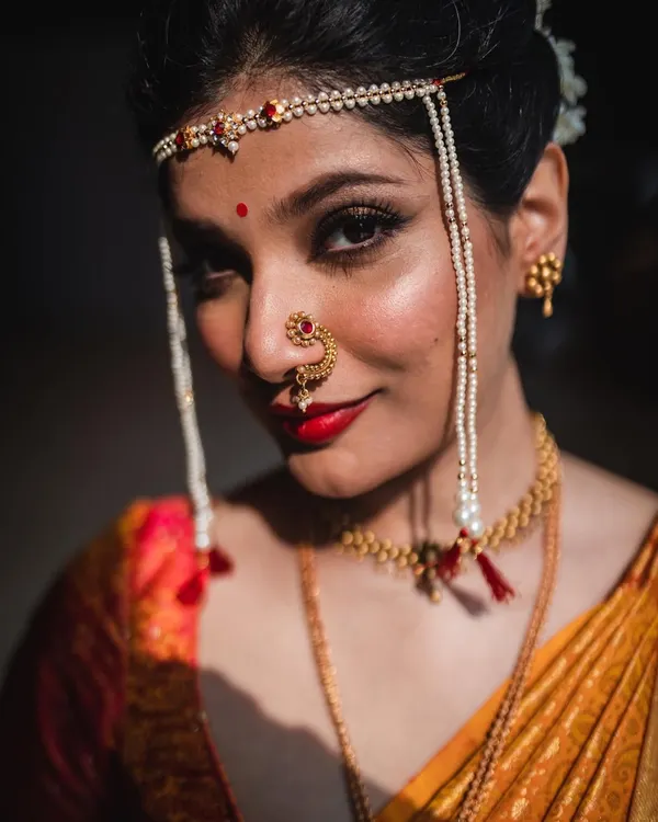A close-up portrait of a Maharashtrian bride, highlighting her traditional jewelry and confident gaze. The lighting is carefully controlled to create a dramatic, painterly effect.