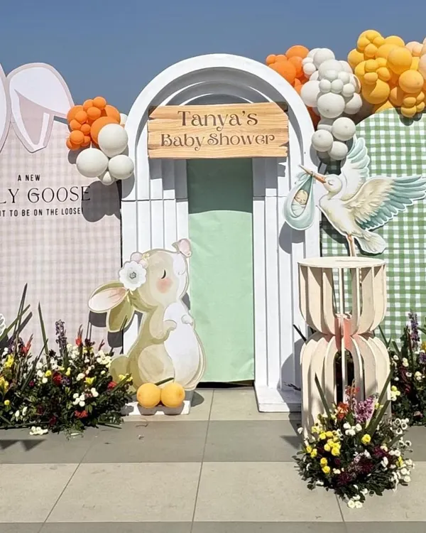 A close-up of the main backdrop for a bunny-themed baby shower. The design features a charming illustration of a bunny and a stork, with a custom wooden sign for 'Tanya's Baby Shower'.