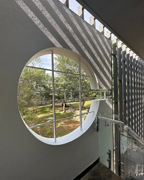 A circular window in the 'Madhuram' project acts as a perfect frame for the landscape outside, while the adjacent slatted screen casts linear shadows.