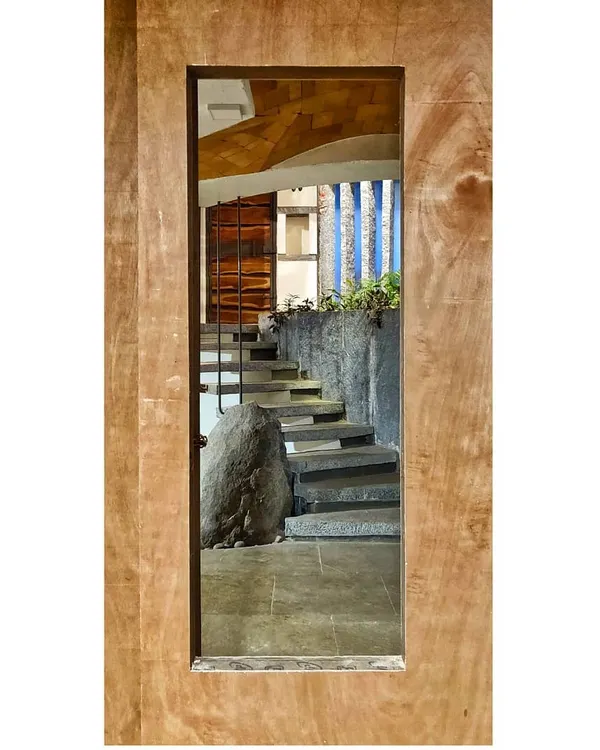 A staircase viewed through a door frame, appearing like a framed piece of art. This composition highlights the raw beauty of the stone steps and the massive boulder at their base, celebrating the power of natural materials.