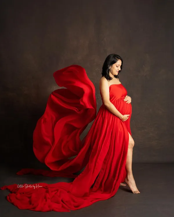 A powerful and elegant portrait of an expecting mother in a flowing red gown. The fabric is captured in motion, creating a dynamic and artistic effect against a classic studio backdrop, celebrating the strength and beauty of pregnancy.