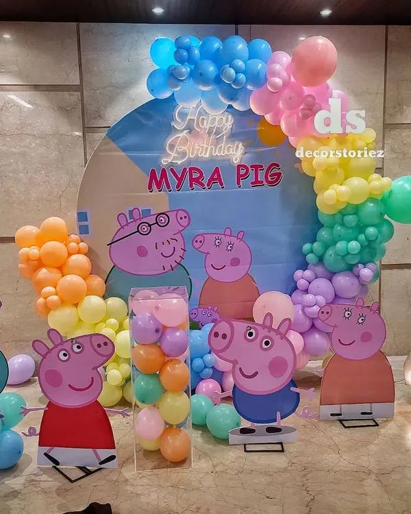 A full view of a Peppa Pig themed birthday party, showcasing multiple character cutouts, a custom backdrop, a light-up number '4', and a colorful pastel balloon arch.