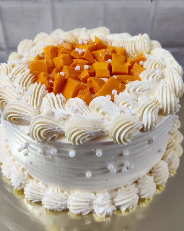 A delicious fresh mango cake. This seasonal favorite is topped with fresh mango chunks and decorated with delicate buttercream piping.