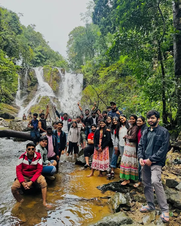 A large, happy group posing in front of a waterfall. This is the community we build every weekend.