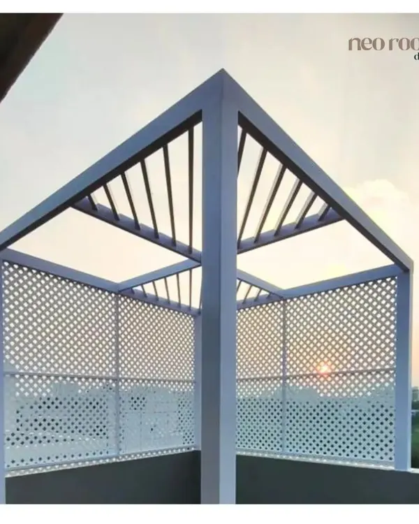 This modern, minimalist pergola on a rooftop features a white metal frame and a slatted roof. The perforated side panels offer partial privacy while creating beautiful light and shadow patterns, perfect for enjoying a sunset view.