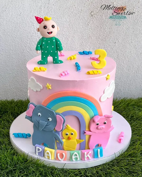This Cocomelon cake is perfect for a toddler's birthday, featuring JJ and his animal friends. The design includes a bright rainbow and other fun, handmade fondant characters on a delicious pink whipped cream cake.