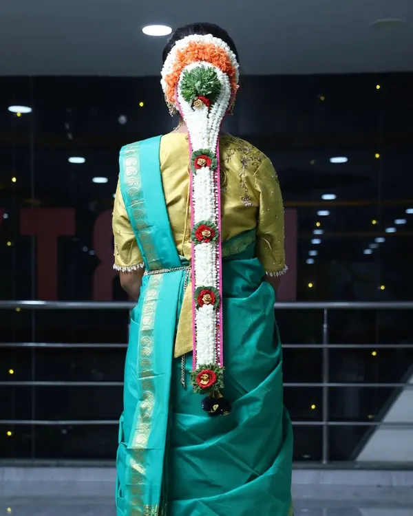 A detailed view of a traditional South Indian bridal braid, adorned with fresh flowers and a central green element, perfect for a Muhurtham.